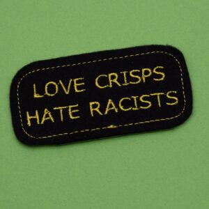 Embroidered iron on patch. Patch is embroidered onto black felt with yellow thread and reads LOVE CRISPS HATE RACISTS