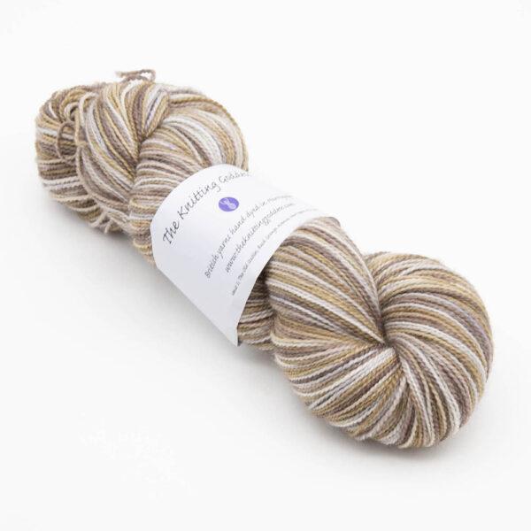 skein of hand dyed pebble yarn in brown, caramel and silver with The Knitting Goddess ball band